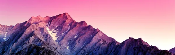 Rocky mountain ridge with patches of snow under a pink and purple dusk sky
